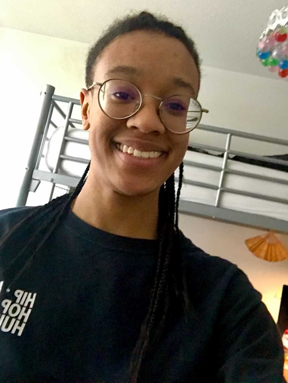 A selfie of Imani wearing a HipHopHuis shirt. She's in her bedroom similing, looking kind of goofy with her glasses on.